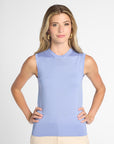 A woman modeling a sleeveless light blue knit top with a crew neck, paired with beige pants, against a plain light gray studio background.