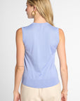 A woman shown from the back wearing a light blue sleeveless knit top and beige pants against a plain light gray studio background.