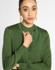 A woman wearing a green long-sleeve knit cardigan with a split neckline and button front, posed against a light gray studio background.