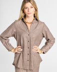 A woman modeling a brown and beige plaid button-up shirt and matching pants set against a light gray studio background.