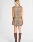 A woman shown from the back wearing a sleeveless tweed vest and matching shorts in a multicolor woven pattern, paired with brown knee-high boots, against a light gray studio background.