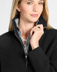 A close-up of a woman wearing a black quarter-zip sweater with a striped black and white inner collar, layered over a black and white striped shirt.