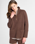 A woman modeling a brown quarter-zip fleece pullover sweater with front patch pockets, paired with matching brown shorts and a striped shirt underneath, against a light gray studio background.