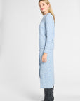 A woman modeling a light blue long-sleeve knit cardigan with a subtle floral pattern, paired with black knee-high boots, photographed against a plain light gray studio background.