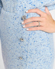 Close-up of a light blue and dark blue speckled knit cardigan with silver buttons, worn by a model whose hand is resting on the front.