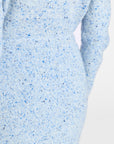 Close-up of a light blue knit sweater with blue and black speckles, showing the ribbed texture and part of the sleeve against a plain white background.