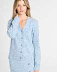 A woman modeling a light blue knit cardigan and matching skirt set with a subtle speckled texture and silver buttons, photographed against a plain light gray studio background.