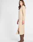 A woman modeling a beige knit sweater and matching midi skirt set with a side slit, paired with brown knee-high heeled boots, against a light gray studio background.