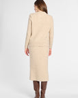 A woman shown from the back wearing a matching beige knit jacket and midi skirt set, paired with brown knee-high boots, against a light gray studio background.