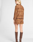 A woman shown from the back wearing a matching tweed jacket and mini skirt set in a warm orange-brown pattern, paired with brown knee-high boots, against a light gray studio background.