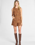 A woman modeling a sleeveless, short romper in a textured multicolor tweed fabric with brown knee-high boots, shot against a light gray studio background.