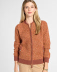 A woman modeling a textured, heathered rust-orange zip-up cardigan with ribbed collar, cuffs, and hem, paired with beige pants, against a light gray studio background.