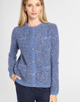 A woman modeling a blue marled knit cardigan sweater with button-front closure and flap pockets, paired with dark navy pants against a light gray studio background.