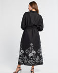 Woman wearing a black dress with floral patterns with black heels on a white background