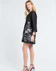 Woman modeling a black dress with white floral patterns on a white background