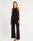 Woman wearing a black sleeveless blouse and wide-leg pants on a white background