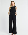 Woman wearing a black sleeveless top and wide-leg pants on a white background