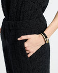 Person wearing a black floral textured outfit with hands in pockets on a white background