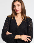 Woman wearing a black v-neck dress with gold jewelry on a white background
