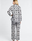 Woman wearing a black and white floral patterned blouse and pants with black heels on a white background