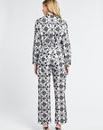 Woman wearing a black and white floral long sleeve blouse and long pants on a white background