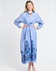 Woman wearing a blue maxi dress with floral embroidery on a white background