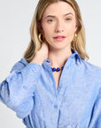 Woman wearing a button down blue dress and necklace with a plain background