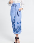 Woman modeling a blue skirt with floral embroidery on a white background