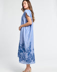 Woman wearing a long blue caftan with floral embroidery on a white background