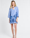 Woman wearing a blue caftan with floral embroidery on a white background
