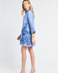 Woman wearing a blue caftan with floral embroidery with white heels on a white background