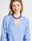 Woman wearing a blue caftan with floral patterns and a blue necklace against a white background