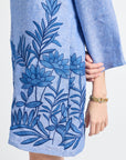woman dressed in a blue caftan with floral embroidery on a white background