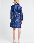 Woman wearing a knee-length navy dress with a silver swirl pattern on a white backdrop