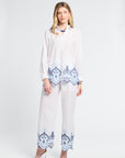 Woman wearing a white blouse and pants with blue embroidery on the trip with a white background