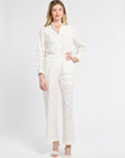 Woman modeling white pants with floral detailing against a white backdrop