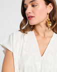 Woman wearing a white dress with gold earrings against a light background