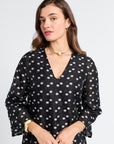 Woman wearing a sheer black dress with white floral pattern on a light gray background