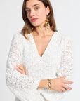 Woman wearing a white lace caftan with gold jewelry on a light gray background