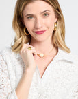 Woman wearing gold jewelry and a white lace blouse against a white background