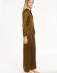 A woman modeling the Golden Umber Eleanor Shirt with coordinating Diane Pants, three-quarter side view, photographed against a plain white studio background.