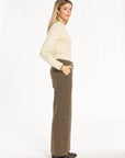 A woman modeling the Tobacco Tweed Ellis Pants with a cream sweater and brown loafers, side view, photographed against a plain white studio background.