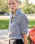 A woman wearing a black and white striped shirt with a collar, rolled sleeves, and button-up front.