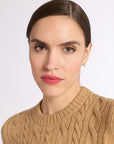 Close up headshot of woman wearing a beige cashmere cable knit crew sweater against a white background