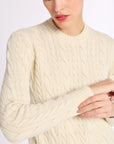 Close up of woman with arms folded wearing a cream cashmere cable knit crew sweater on a white background