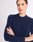 Woman with arms folded wearing a navy cashmere cable knit crew sweater on a white background