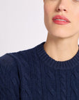 Close-up of a woman wearing a navy cashmere cable knit crew sweater against a white background