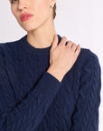 Close up of woman with hand on should wearing a navy cashmere cable knit crew sweater on a white background