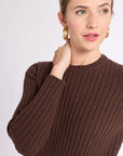 Close up of woman with hand on shoulder wearing brown ribbed sweater and skirt