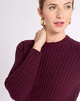 Woman with hand on shoulder wearing burgundy ribbed crew sweater against white background
